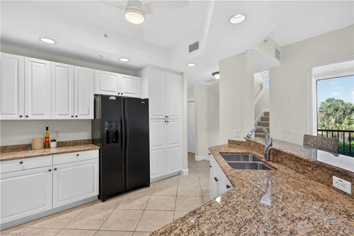 Kitchen featuring white cabinetry, dark stone counters, black fridge, light tile patterned flooring, and recessed lighting