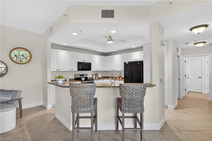Kitchen with white cabinetry, dark stone counters, black appliances, a raised ceiling, and ceiling fan