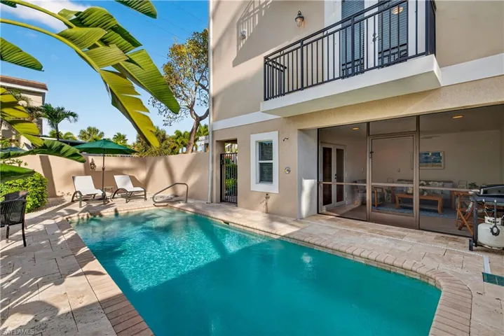 View of swimming pool featuring a balcony, patio surround, a sunroom, and french doors