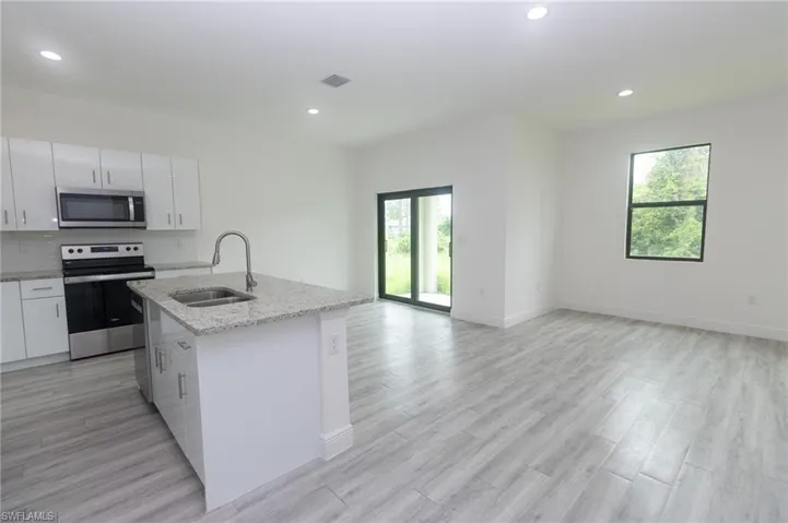 Kitchen featuring appliances with stainless steel finishes, an island with sink, white cabinetry, light hardwood / wood-style flooring, and sink