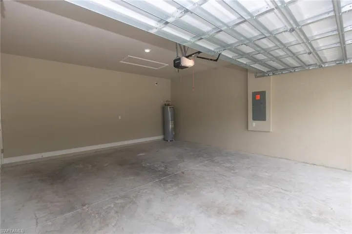Garage with water heater, electric panel, and a garage door opener