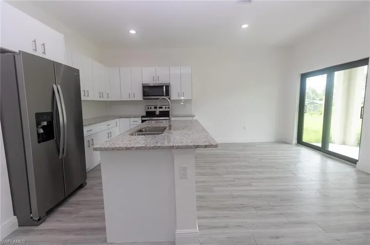 Kitchen with light stone counters, stainless steel appliances, a kitchen island with sink, and white cabinetry