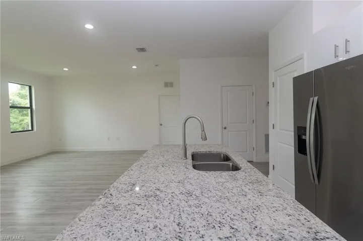 Kitchen featuring light stone countertops, white cabinetry, stainless steel fridge, light hardwood / wood-style flooring, and sink