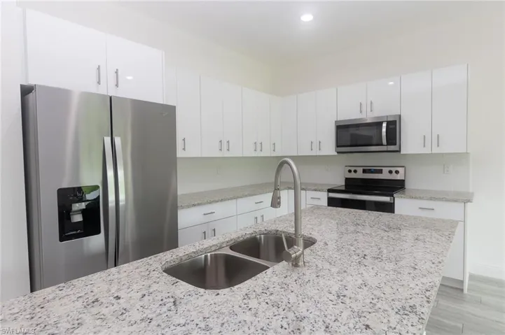 Kitchen featuring appliances with stainless steel finishes, white cabinets, and light stone countertops