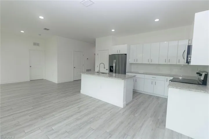 Kitchen featuring appliances with stainless steel finishes, light hardwood / wood-style floors, white cabinets, and a kitchen island with sink