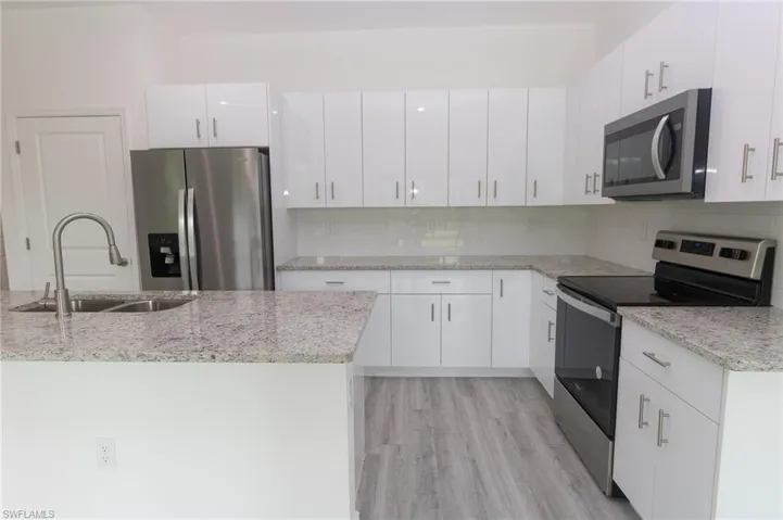 Kitchen with white cabinetry, appliances with stainless steel finishes, light wood-type flooring, tasteful backsplash, and sink