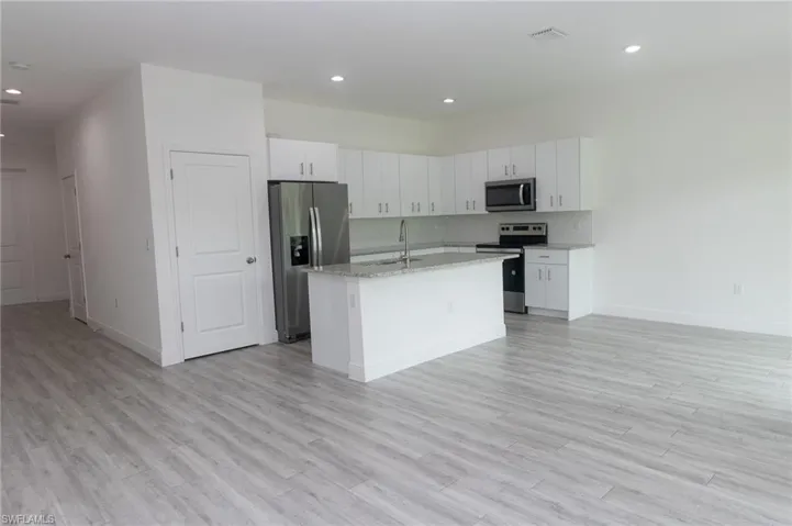 Kitchen with a center island with sink, appliances with stainless steel finishes, light hardwood / wood-style floors, light stone countertops, and white cabinetry