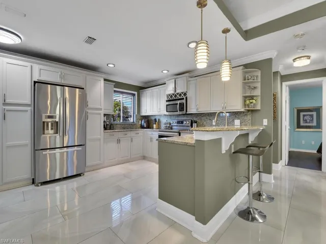 Kitchen featuring backsplash, light stone counters, stainless steel appliances, decorative light fixtures, and white cabinets