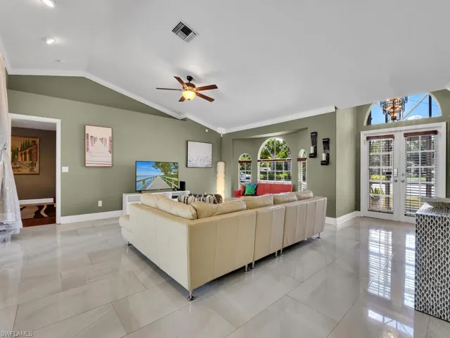Tiled living room featuring ceiling fan, french doors, crown molding, and vaulted ceiling
