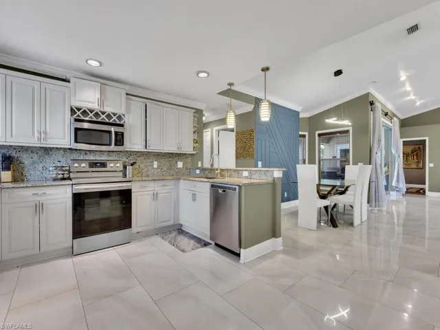 Kitchen with pendant lighting, ornamental molding, tasteful backsplash, kitchen peninsula, and stainless steel appliances