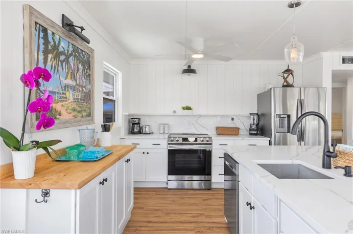 Kitchen with appliances with stainless steel finishes, ceiling fan, sink, decorative light fixtures, and white cabinetry