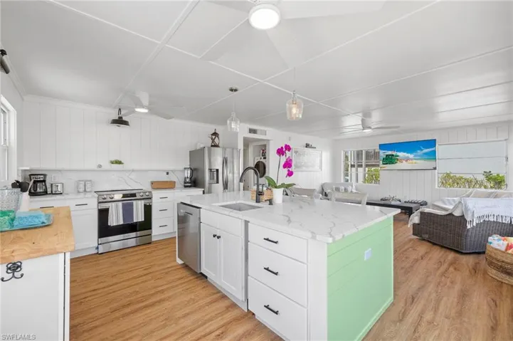 Kitchen featuring white cabinetry, sink, stainless steel appliances, a kitchen island with sink, and light wood-type flooring