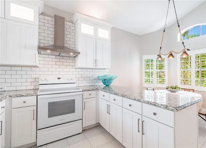 Kitchen featuring white range with electric cooktop, wall chimney range hood, light stone counters, and white cabinetry