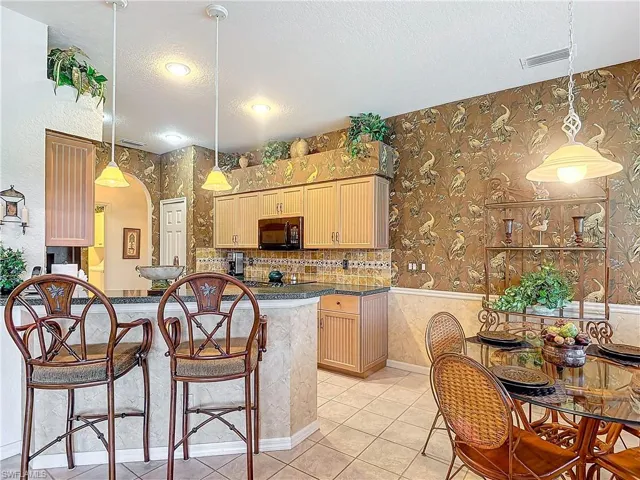 Kitchen with light brown cabinets, a textured ceiling, decorative light fixtures, and black appliances