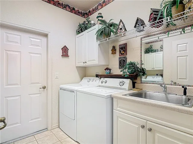 Laundry area featuring light tile patterned flooring, sink, washing machine and clothes dryer, and cabinets