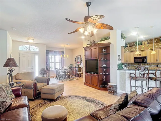 Living room with light wood-type flooring, ceiling fan with notable chandelier, and a textured ceiling