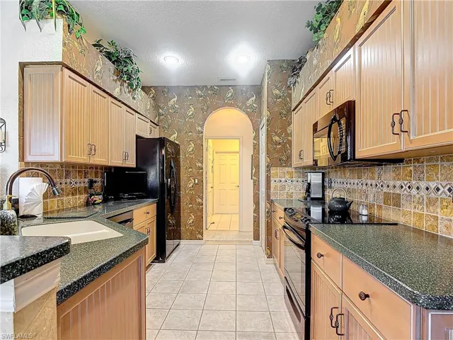 Kitchen with a textured ceiling, sink, backsplash, black appliances, and light tile patterned floors