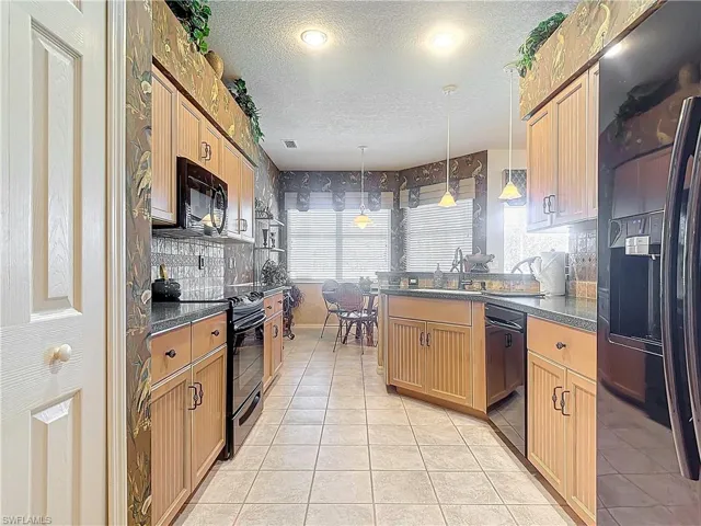 Kitchen with light tile patterned flooring, sink, a textured ceiling, decorative light fixtures, and black appliances