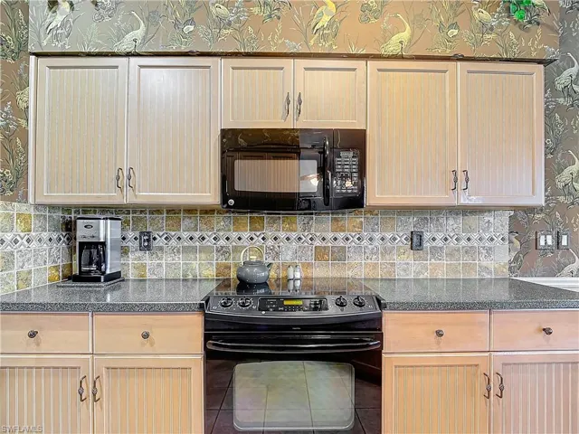Kitchen featuring light brown cabinets, decorative backsplash, and black appliances
