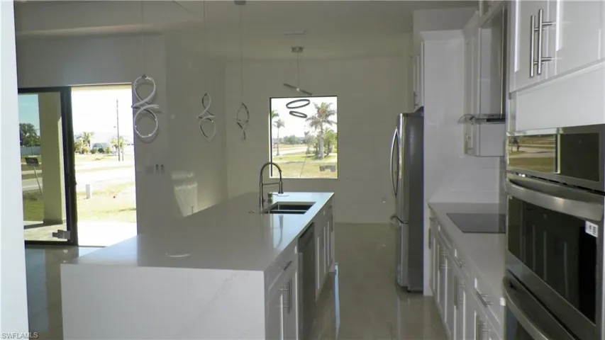 Kitchen featuring pendant lighting, an island with sink, white cabinets, stainless steel appliances, and a sink