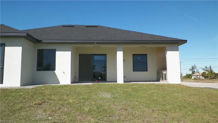 Back of property with a shingled roof, a yard, and stucco siding