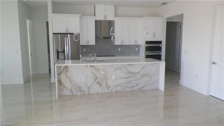 Kitchen featuring a kitchen island with sink, appliances with stainless steel finishes, white cabinetry, wall chimney exhaust hood, and a sink