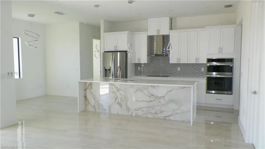Kitchen featuring wall chimney range hood, an island with sink, appliances with stainless steel finishes, white cabinetry, and a sink
