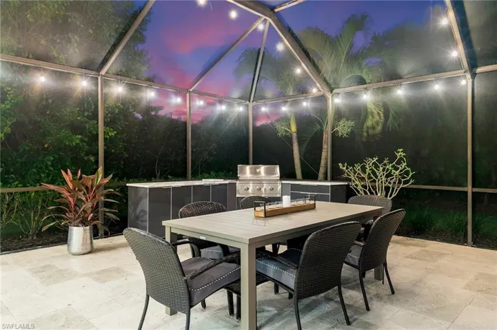 Patio terrace at dusk with exterior kitchen, a lanai, and a grill