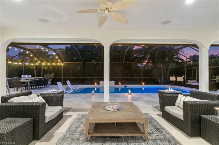Pool at dusk featuring a patio area, glass enclosure, an outdoor hangout area, and ceiling fan