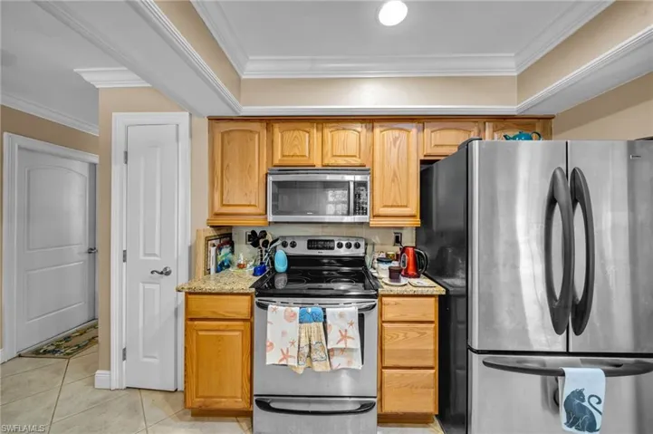 Kitchen featuring light stone counters, light tile patterned flooring, appliances with stainless steel finishes, and ornamental molding