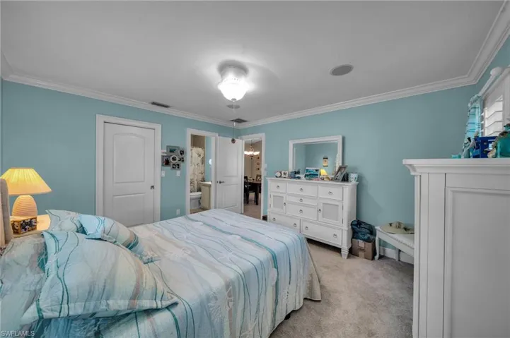 Bedroom with visible vents, light carpet, ornamental molding, and ensuite bathroom