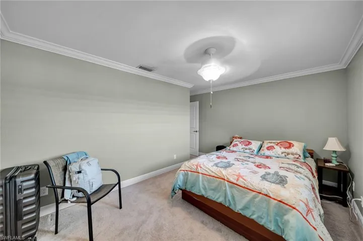 Carpeted bedroom with visible vents, baseboards, ceiling fan, and crown molding
