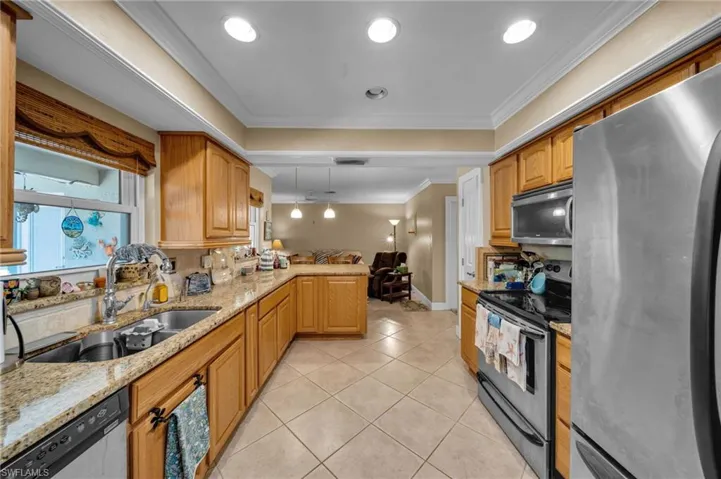 Kitchen with ornamental molding, a sink, a peninsula, appliances with stainless steel finishes, and light tile patterned flooring