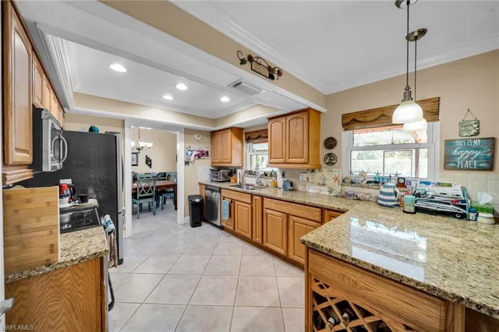 Kitchen with light stone counters, light tile patterned floors, ornamental molding, stainless steel appliances, and a chandelier