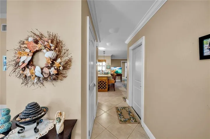 Hallway with light tile patterned floors, visible vents, and crown molding