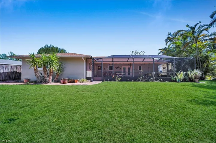 Back of house with a lanai, stucco siding, a lawn, and fence