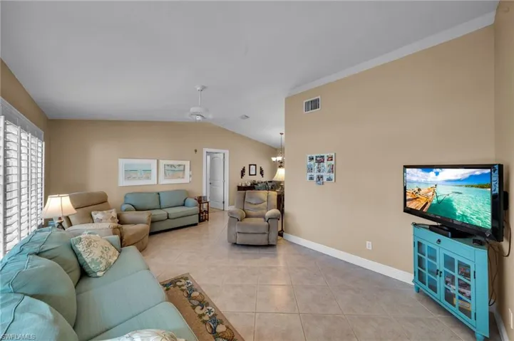 Living room featuring light tile patterned floors, a ceiling fan, visible vents, baseboards, and lofted ceiling