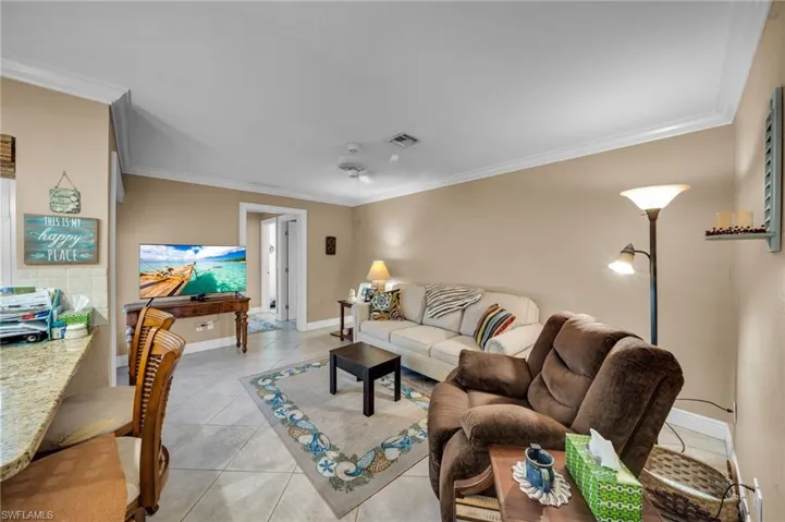 Living room with light tile patterned floors, visible vents, baseboards, and crown molding