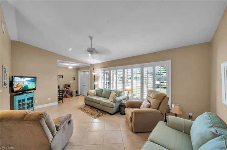 Living area featuring light tile patterned floors, baseboards, ceiling fan, and vaulted ceiling