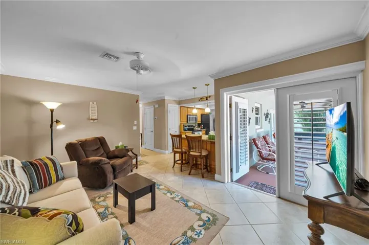 Living area featuring light tile patterned floors, visible vents, and crown molding