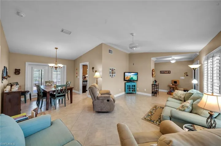 Living room featuring light tile patterned floors, baseboards, visible vents, an inviting chandelier, and vaulted ceiling