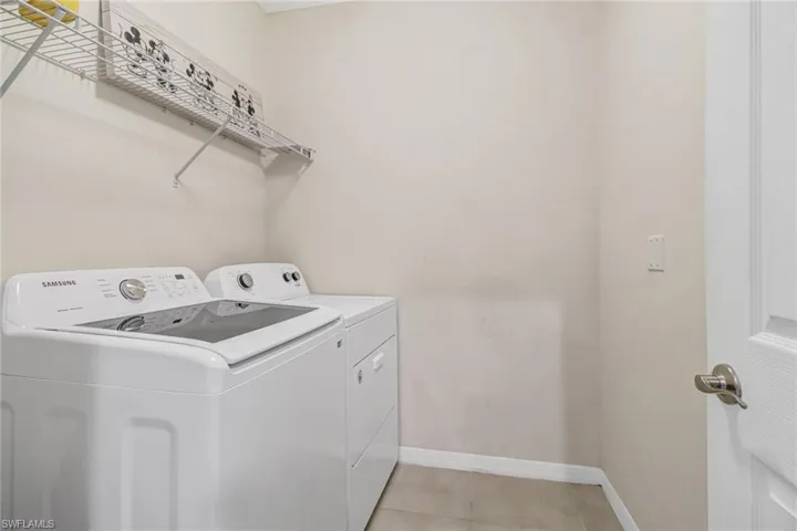Washroom with washing machine and clothes dryer and light tile patterned floors