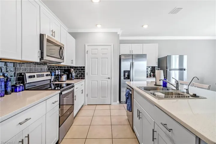 Kitchen with tasteful backsplash, light tile patterned flooring, stainless steel appliances, and white cabinetry