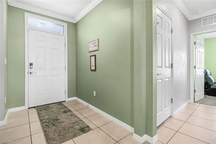Foyer entrance with light tile patterned floors and crown molding