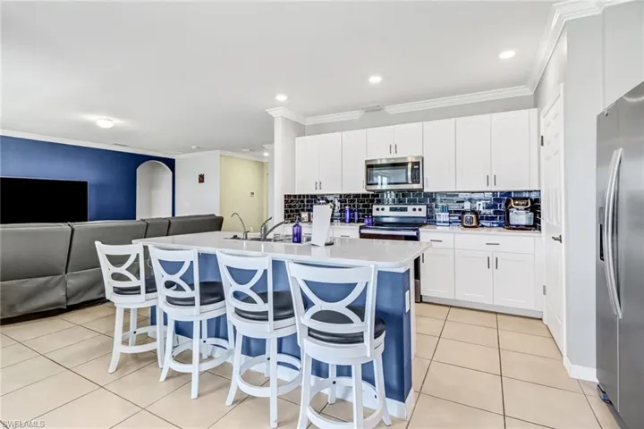 Kitchen with appliances with stainless steel finishes, light tile patterned floors, an island with sink, tasteful backsplash, and a breakfast bar