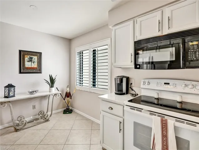 Kitchen with electric range, white cabinetry, black microwave, light tile patterned flooring, and light stone countertops