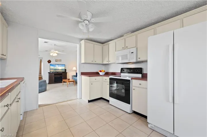 Kitchen with light colored carpet, ceiling fan, white appliances, and a textured ceiling