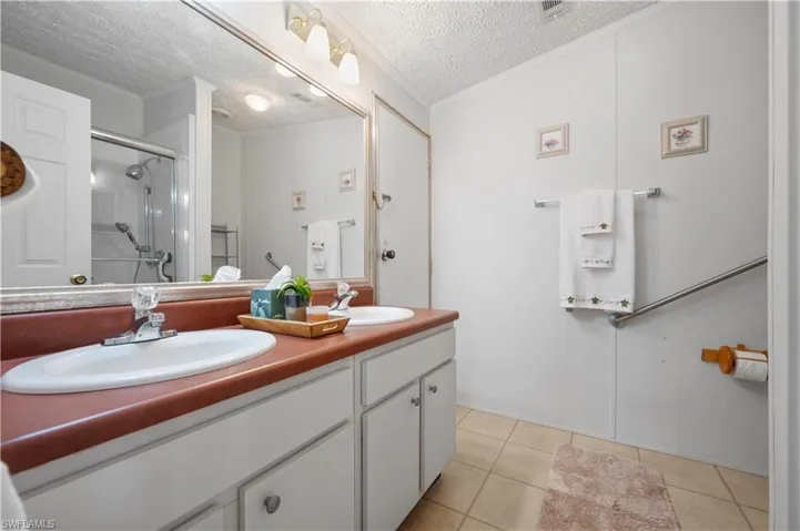 Bathroom featuring crown molding, a textured ceiling, tile flooring, and dual bowl vanity