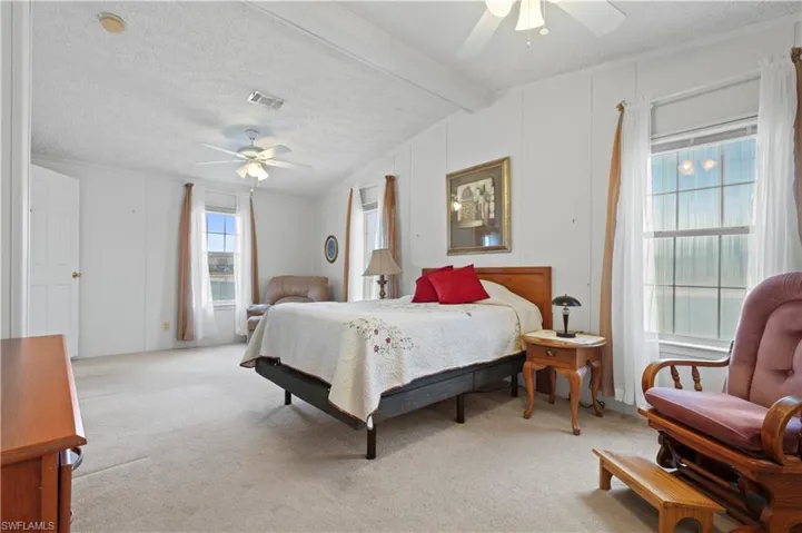 Carpeted bedroom with vaulted ceiling, ceiling fan, and a textured ceiling