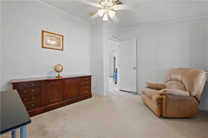 Living area with ceiling fan, a textured ceiling, and light colored carpet